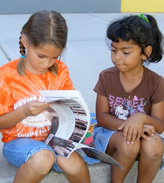 Two students flip the pages of a book outside